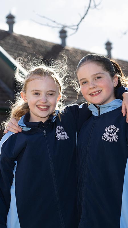 Our Lady of the Nativity Primary Lawson students smiling outdoors. The mural is in the background.