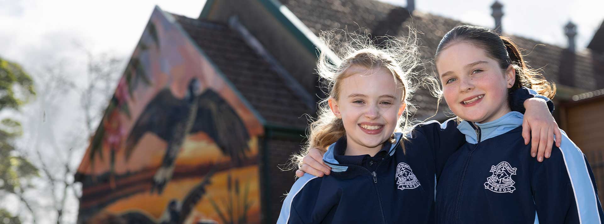 Our Lady of the Nativity Primary Lawson students smiling outdoors. The mural is in the background.