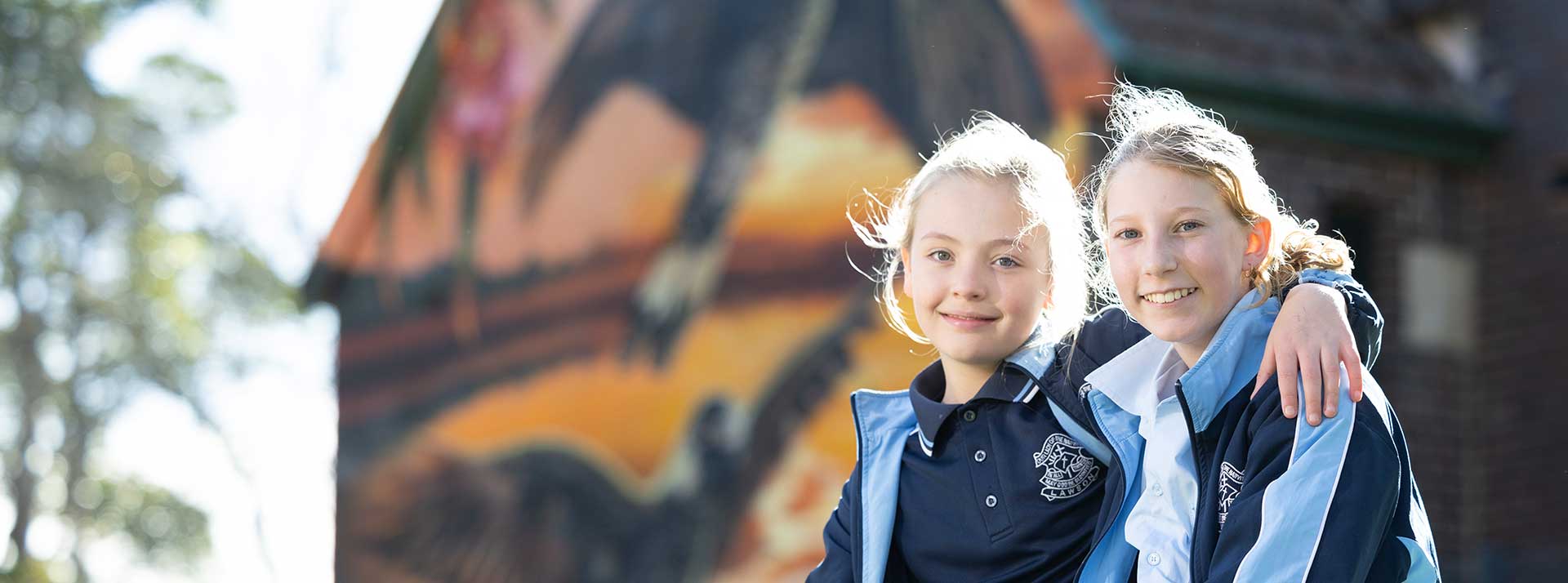 Our Lady of the Nativity Primary Lawson students smiling outdoors. The mural is in the background.