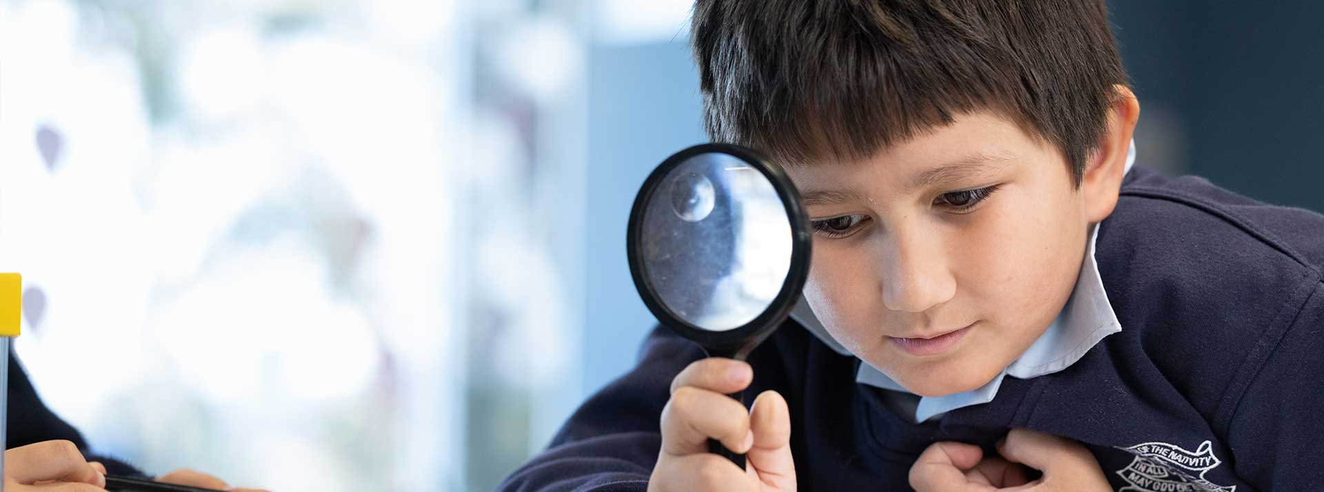 Our Lady of the Nativity Primary Lawson student in class. He is using a magnifying glass.