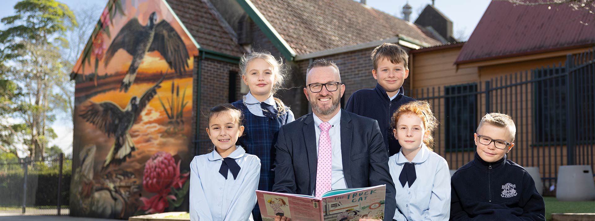Matthew Bond, Principal of Our Lady of the Nativity Primary Lawson, reading to students in an outdoor setting.