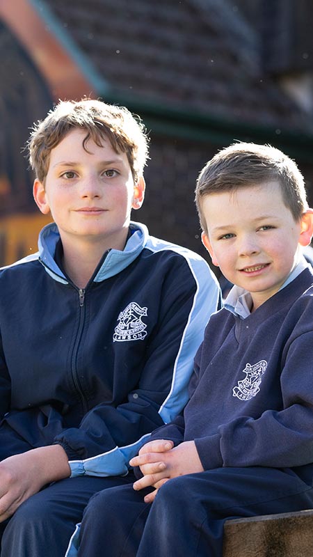Two Our Lady of the Nativity Lawson students sitting outdoors. The school Church is in the background.