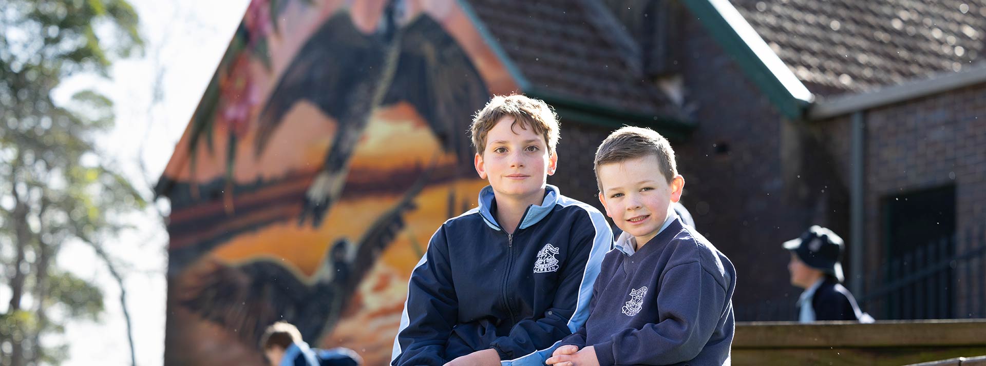 Two Our Lady of the Nativity Lawson students sitting outdoors. The school Church is in the background.