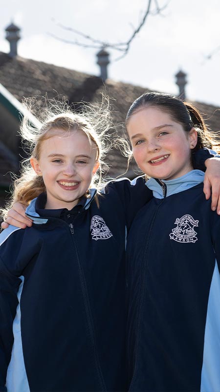 Two smiling OLN Lawson students outdoors. The Church and Mural is in the background.