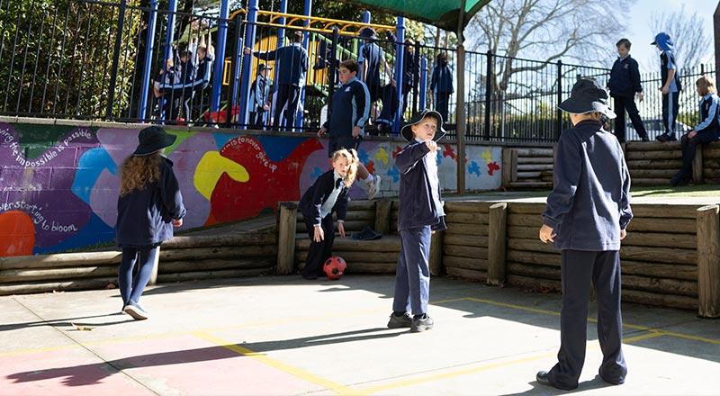 Before and after school care at Our Lady of the Nativity, Lawson. The students are playing soccer, and the playground equipment (Slides, monkey bars) is in the background.
