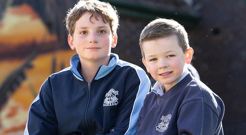 Two Our Lady of the Nativity Lawson students sitting outdoors. The school Church is in the background.
