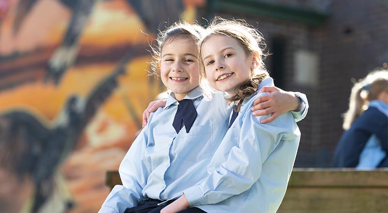 Two OLN Lawson students sitting outdoors. They are smiling and have their arms wrapped around each other.