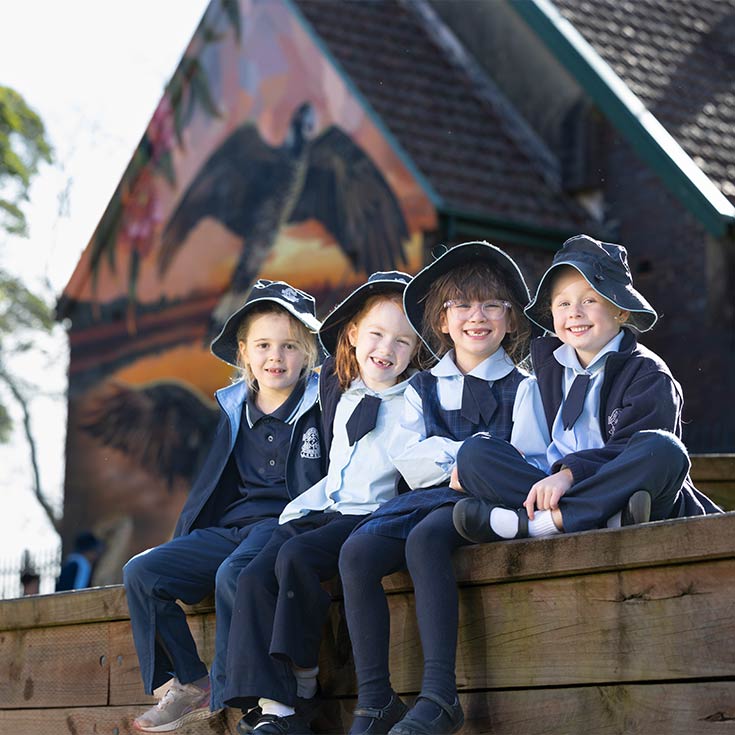 Four smiling OLN Lawson students outdoors. The Church and Mural is in the background.
